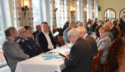 Eine Gruppe von Menschen, darunter einige in deutscher Militäruniform, sitzt an einem langen Tisch bei einer formellen Veranstaltung.