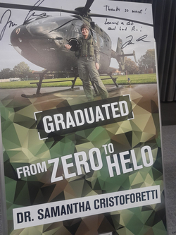 Dr. Samantha Cristoforetti im Fliegeranzug lächelt neben einem Militärhubschrauber. Text: 'GRADUATED FROM ZERO TO HELO'.