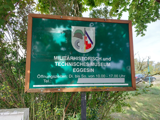Grünes Schild des Militärhistorischen und Technischen Museums Eggesin mit Öffnungszeiten: Di. bis So. von 10-17 Uhr.