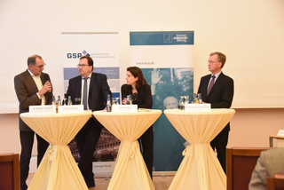 Vier Diskussionsteilnehmer (3 Männer, 1 Frau) an Stehtischen. GSP- und Konrad-Adenauer-Stiftung-Banner im Hintergrund.