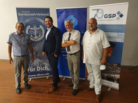 Vier Männer lächeln vor Bannern des Deutschen BundeswehrVerbandes und der Gesellschaft für Sicherheitspolitik (GSP).