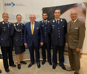 Gruppe: vier junge Leute in Bundeswehr-Uniformen und zwei Männer in Anzügen, vor einem Banner der Gesellschaft für Sicherheitspolitik.