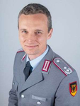 Ein lächelnder deutscher Soldat, Bohnert, in grauer Bundeswehruniform mit Dienstgradabzeichen und Hoheitszeichen.