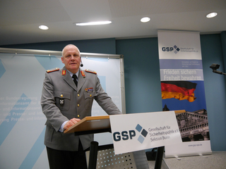 Deutscher Offizier General Spannuth spricht bei einem GSP-Event an einem Rednerpult vor Bannern in Uniform.