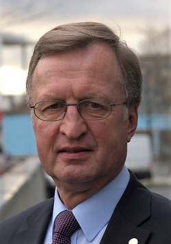 Nahaufnahme-Porträt eines Mannes mittleren Alters mit Brille, hellbraunem Haar, Anzug und Krawatte, blickt direkt in die Kamera.