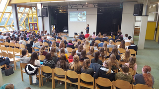 Ein junger Mann präsentiert vor einem großen Publikum von Schülern in einem Auditorium mit einer Folie über Weltraumschrott.
