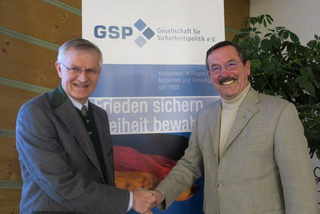 Zwei lächelnde Männer schütteln sich die Hände vor einem GSP-Banner mit den Farben der deutschen Flagge.