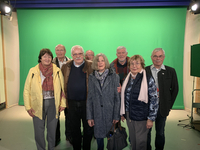 Acht Senioren (fünf Männer, drei Frauen) posieren in einem TV-Studio vor einem Greenscreen.