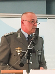 Offizier der Bundeswehr in olivgrüner Uniform mit Brille und Abzeichen spricht an einem Rednerpult ins Mikrofon.