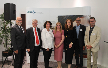 Gruppenfoto von sieben lächelnden Personen (vier Männer, drei Frauen) vor einem GSP-Banner bei einer Veranstaltung.