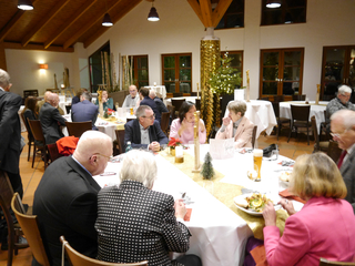 Gruppe von Menschen bei einem festlichen Abendessen in einem dekorierten Raum, wahrscheinlich zu Weihnachten, unterhalten sich und essen.