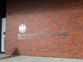 Backsteinwand des Bundesnachrichtendienst Besucherzentrums mit Bundesadler-Emblem, Schriftzug und Hausnummer 57.