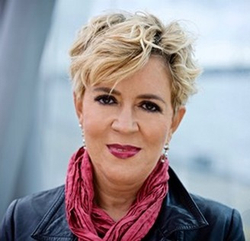 Porträt einer Frau mit kurzen blonden Haaren, dunklem Lippenstift, schwarzer Lederjacke und rosa Schal.