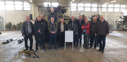 Gruppe Männer posiert mit einem Schützenpanzer Marder, Militärausrüstung und einer Infotafel in einem großen Hangar.