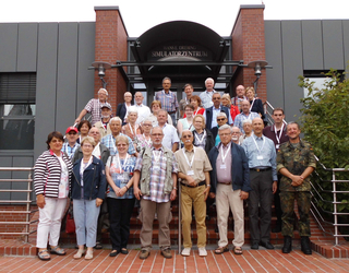 Große Gruppe meist älterer Erwachsener posiert auf den Stufen vor dem Hans E. Drebing Simulatorzentrum für ein Gruppenfoto.