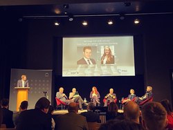 Paneldiskussion mit Sprecher am Pult, fünf Podiumsgästen und Publikum, im Hintergrund eine Präsentation des 'Junge GSP' Teams.