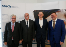 Vier Männer in Anzügen lächeln vor einem GSP (Gesellschaft für Sicherheitspolitik) Banner mit deutschem Text.