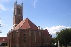 Eine große Backsteinkirche mit hohem Turm, rotem Ziegeldach und Bogenfenstern unter blauem Himmel.