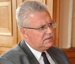 Ein mittelalter Mann mit grauem Haar, Brille und Schnurrbart, Anzug und Krawatte, blickt nach rechts.