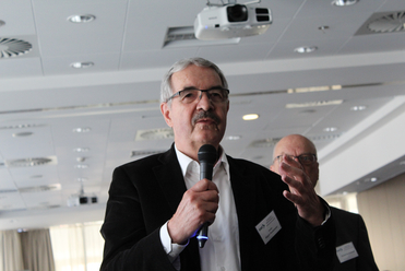 Jürgen Hockemeler, ein Mann mit Brille und Schnurrbart, spricht auf einer Veranstaltung ins Mikrofon.