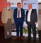 Drei Männer in Anzügen stehen vor Bannern der Gesellschaft für Sicherheitspolitik und des deutschen Reservistenverbandes.