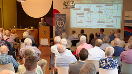Ein Militäroffizier präsentiert die 'Fähigkeiten der Pioniertruppe' vor einem Publikum älterer Erwachsener auf einem Bildschirm.