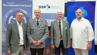Vier Männer, einer davon in Bundeswehr-Uniform, stehen vor Bannern des Deutschen BundeswehrVerbandes und der GSP.