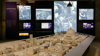 Museumsausstellung mit detailliertem Modell von 'Germania' und Tafeln über NS-Verbrechen wie Konzentrationslager und Zwangsarbeit.