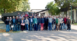 Eine Gruppe von Männern und Frauen posiert vor einem militärischen Kettenfahrzeug mit Kanone und dem Bundeswehr-Kreuz.