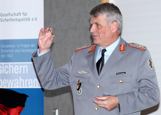 General Hannemann in deutscher Militäruniform spricht, ein kleines Objekt haltend. Ein Banner der "Gesellschaft für Sicherheitspolitik" ist sichtbar.