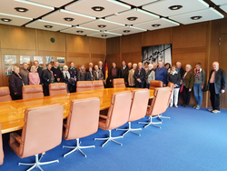 Gruppe von Erwachsenen posiert in einem modernen Konferenzraum mit langem Holztisch und braunen Stühlen, eine Person in Uniform.