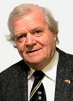 Walther Tröger, ein lächelnder älterer Mann mit grauem Haar, Anzug, Krawatte mit Olympischen Ringen und deutscher Flaggennadel.