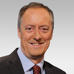 Porträt des deutschen Politikers Friedrich Merz, lächelnd in dunklem Anzug, hellblauem Hemd und rot gepunkteter Krawatte.