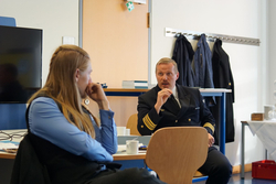 Offizier in Marineuniform spricht mit langhaariger Frau an einem Tisch während eines Meetings.