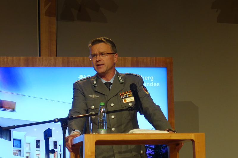 André Wüstner, ein Militäroffizier in Uniform, spricht an einem Rednerpult mit Mikrofon. Im Hintergrund ein blauer Bildschirm.