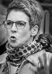 Monochromes Porträt einer Frau mit Brille und kurzen Haaren, die mit geöffnetem Mund lebhaft spricht.