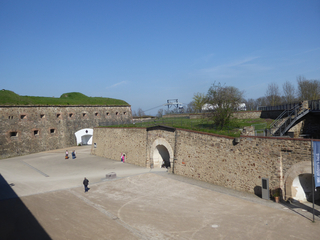 Panoramablick auf die Festung Ehrenbreitstein mit ihren Steinmauern, dem großen Vorplatz, Besuchern und der Seilbahn.