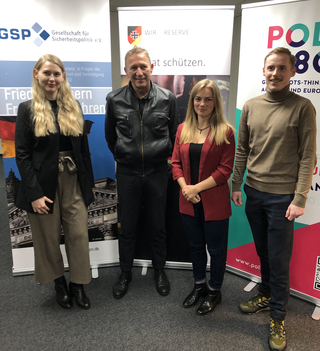 Gruppenfoto von vier Personen (zwei Frauen, zwei Männer) vor Info-Bannern von Sicherheits- und Europapolitik-Organisationen.