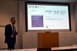 Mann im Anzug präsentiert über maritime Strategie und die Kiel Seapower Series des Instituts für Sicherheitspolitik der Universität Kiel.