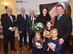 Gruppenfoto: drei Männer, eine Frau und drei Mädchen mit Schokolade und Blumenstrauß vor einem GSP-Banner.