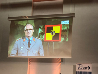 Militäroffizier auf Projektionsfläche mit Adlerwappen und GSP 70 Jahre Jubiläumslogo.