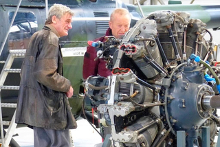 Zwei Männer begutachten einen großen, komplexen Sternmotor eines Flugzeugs. Einer lächelt, der andere blickt auf die Maschine.