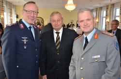 Drei Männer bei einer Veranstaltung: zwei in Militäruniform (blau, grau) und ein älterer Herr im Anzug.