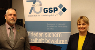 Ein Mann und eine Frau vor einem GSP-Banner zum 70-jährigen Jubiläum der Gesellschaft für Sicherheitspolitik.
