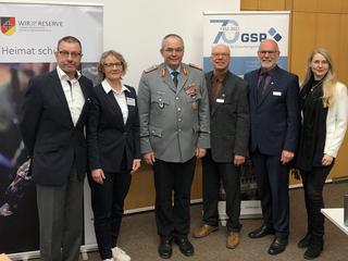 Sechs Personen, darunter ein Offizier der Bundeswehr, posieren bei einem Event mit Bannern der Reserve und GSP.