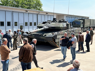 Leopard 2 Kampfpanzer und Militär-LKW auf einem Außengelände, umringt von interessierten Zuschauern.