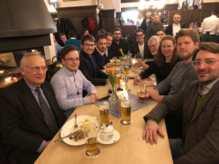 Eine Gruppe von Menschen sitzt an einem Tisch in einer traditionellen Gaststätte, isst und trinkt Bier.