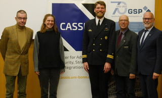 Fünf Personen, darunter ein Marineoffizier, lächeln vor den Bannern von CASSIS und GSP.