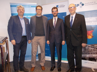Vier lächelnde Männer stehen nebeneinander vor Bannern der Konrad-Adenauer-Stiftung und der Gesellschaft für Sicherheitspolitik.