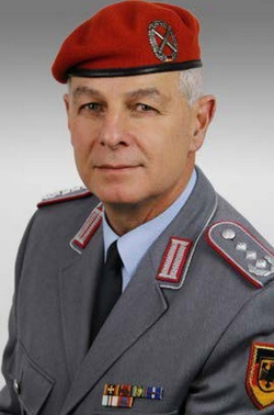 Portrait eines deutschen Bundeswehr-Offiziers in grauer Uniform und rotem Barett, mit Rangabzeichen und Ordensbändern.